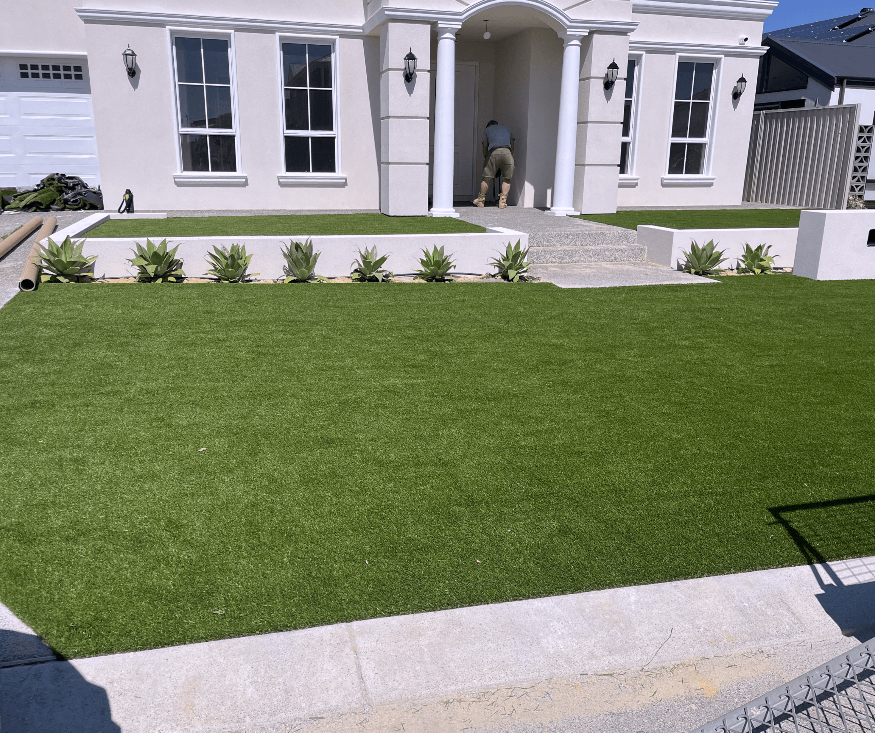 Wide artificial front lawn in front of a white rendered house with a row of agaves